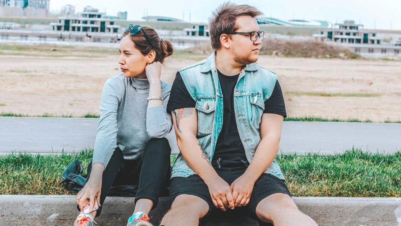 A woman and a man sit on a curb, looking away from each other in opposite directions..