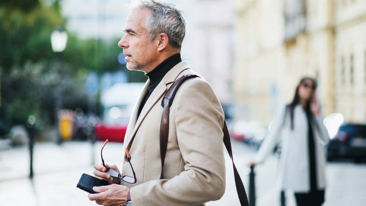 A handsome mature man looks away from a woman talking on the phone in the background.