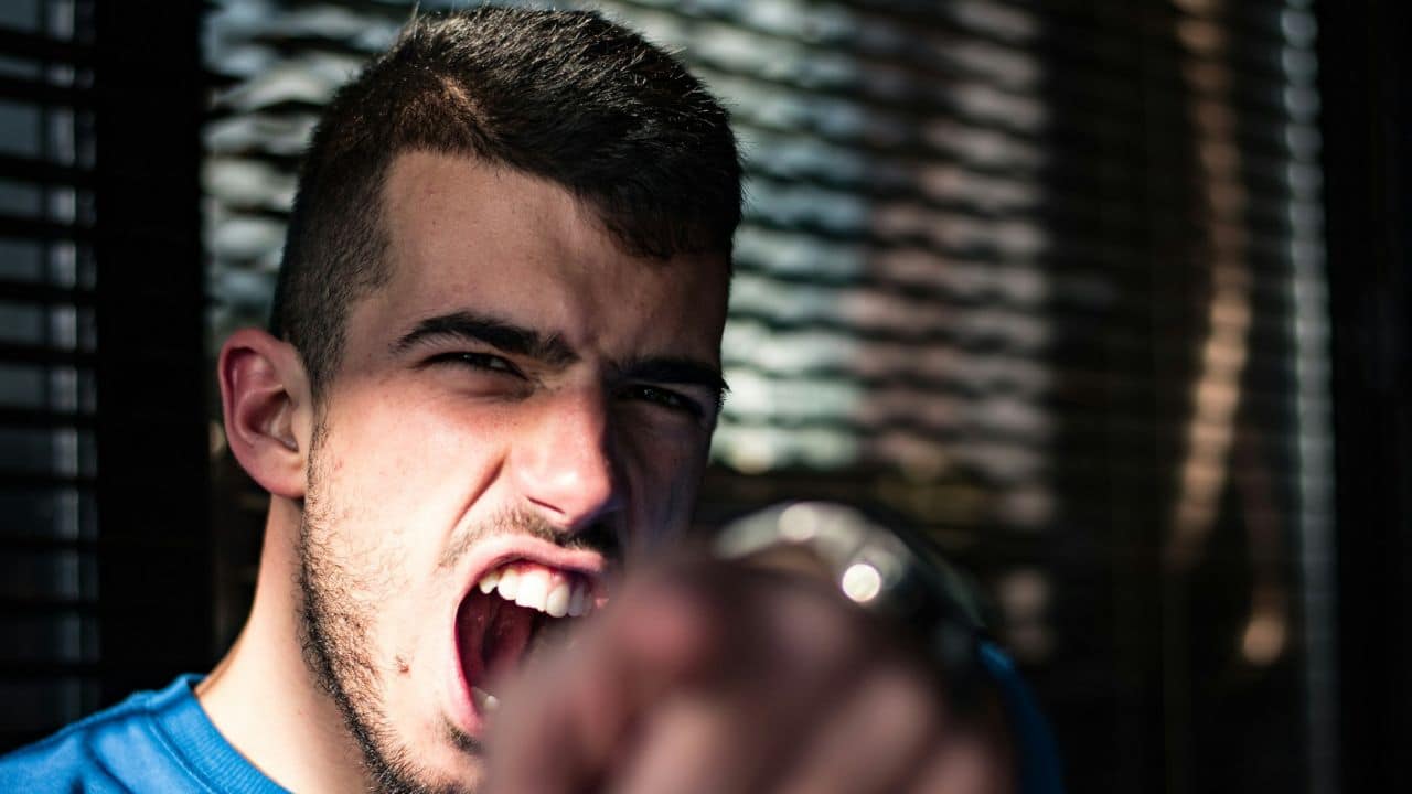 A very angry man with a beard and mustache yells and points at the camera.