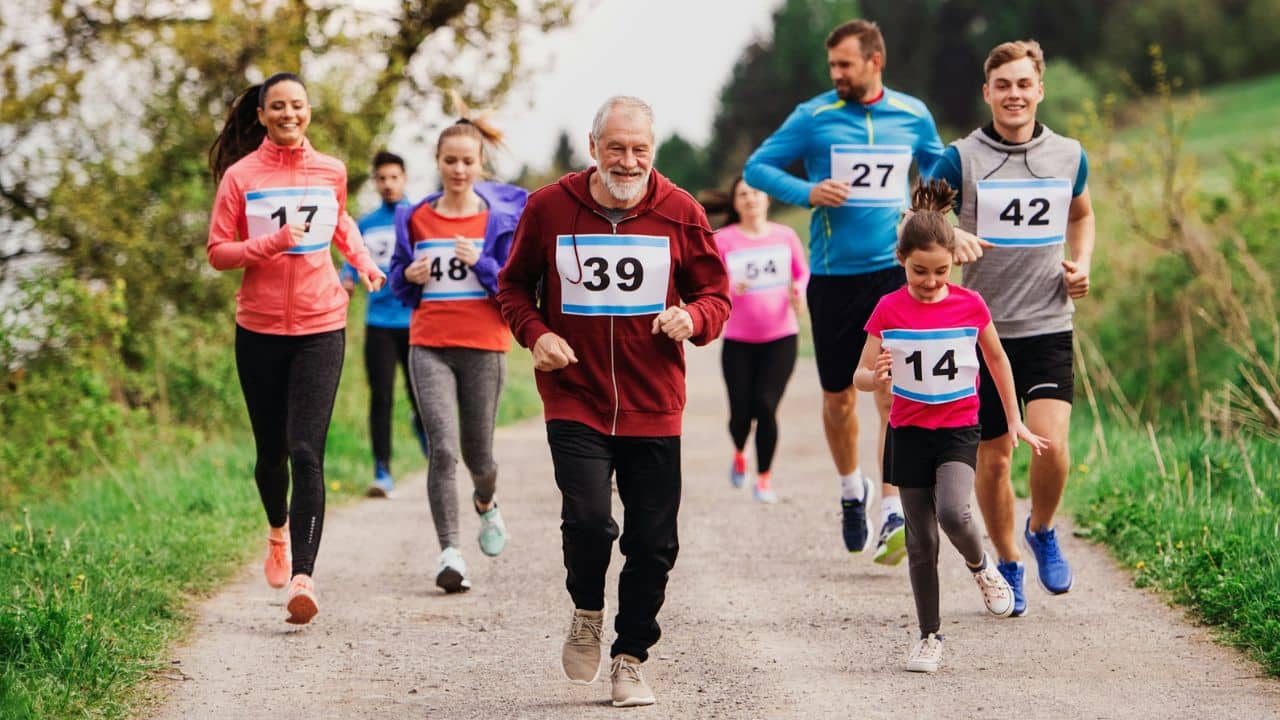 A diverse group of people of all ages runs in a race together outside.