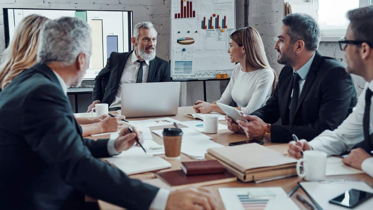 A team of professionals discusses business around a conference table in an office.