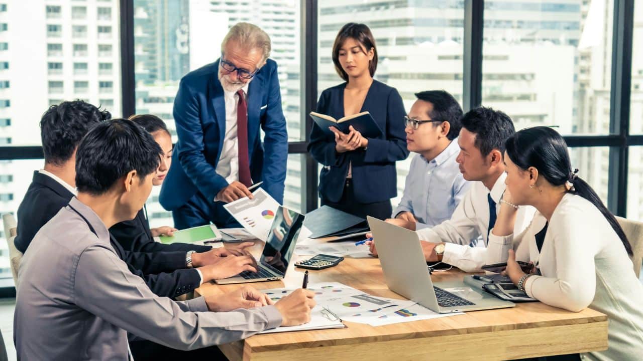 A senior male manager mentors a team of diverse professionals around a conference table.