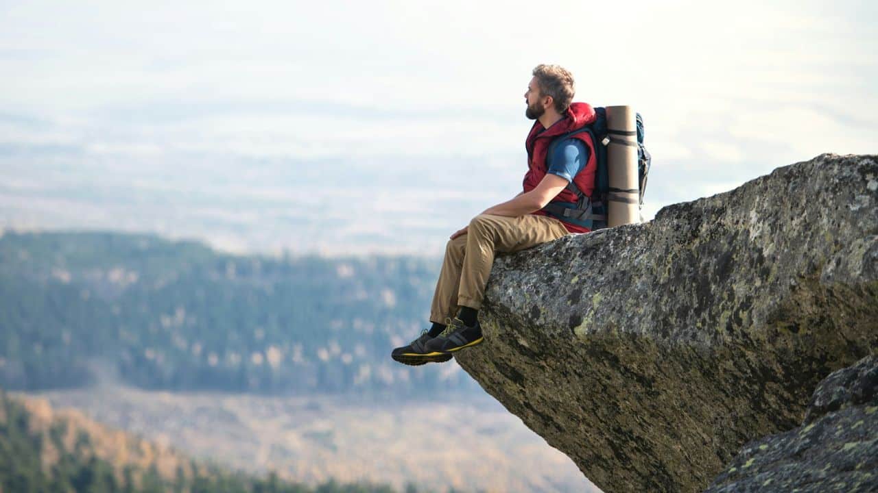 A male hiker sits on the edge of a rock cliff, looking at the view.