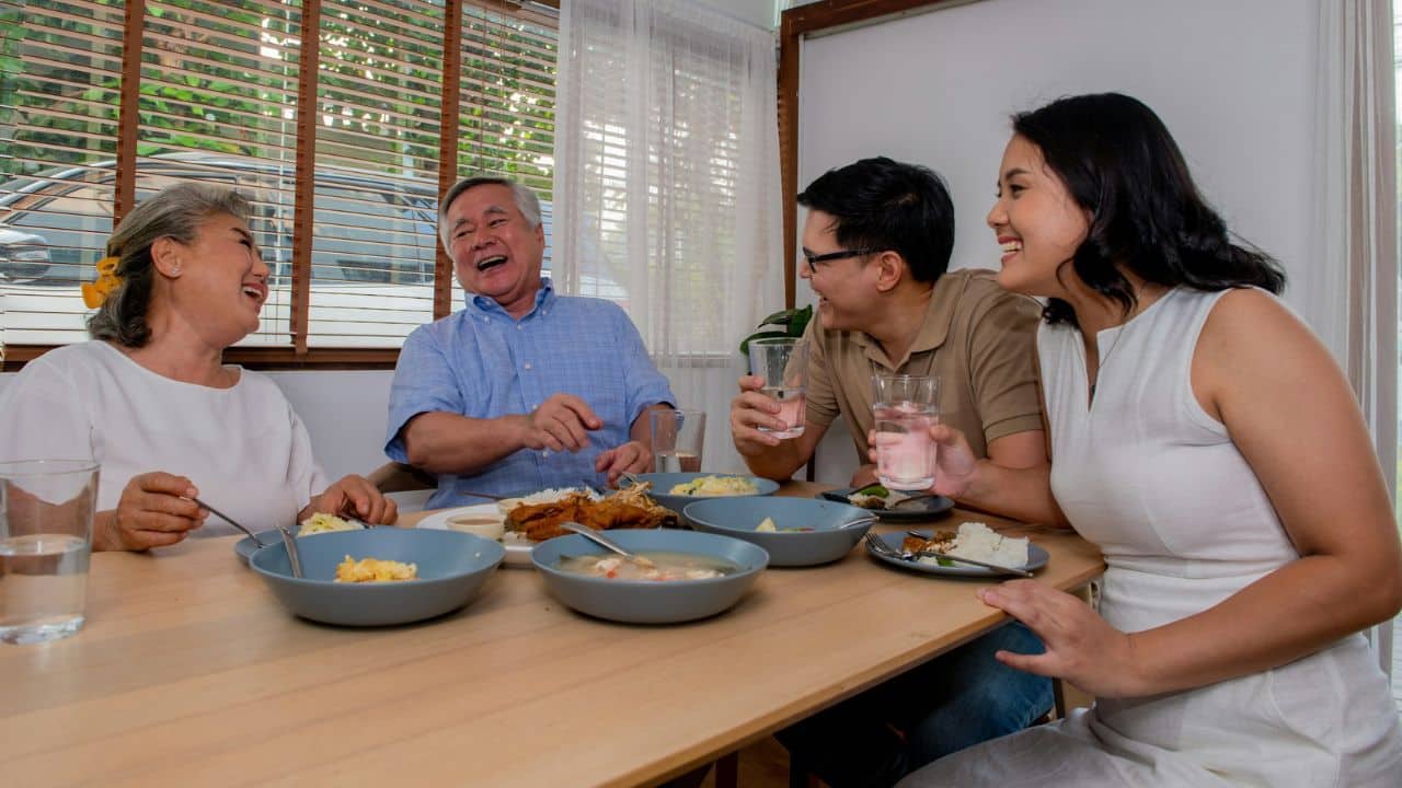 A happy Asian family with two generations is eating and laughing together at a dining table.
