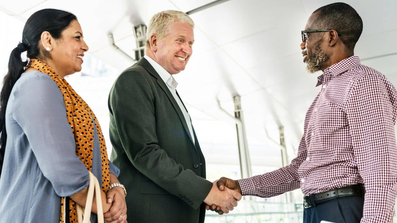 Three smiling professionals of diverse ages and ethnicities are shaking hands.