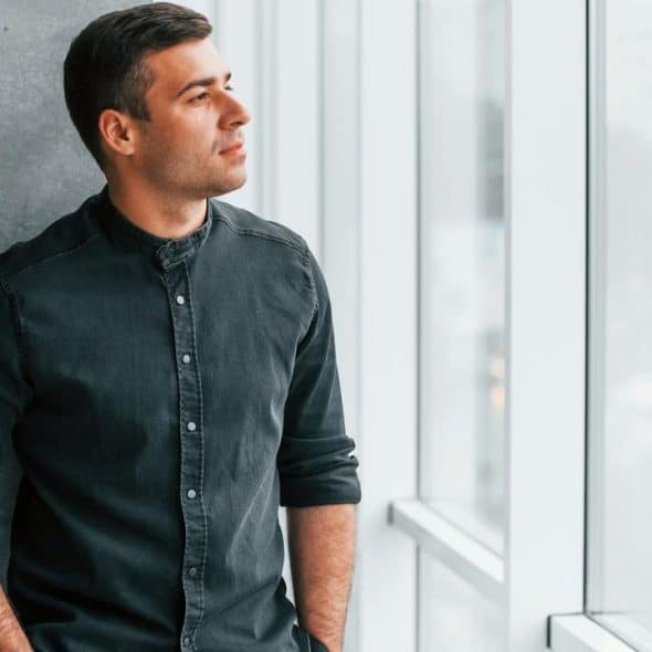 A man in a dark shirt looking out a window.