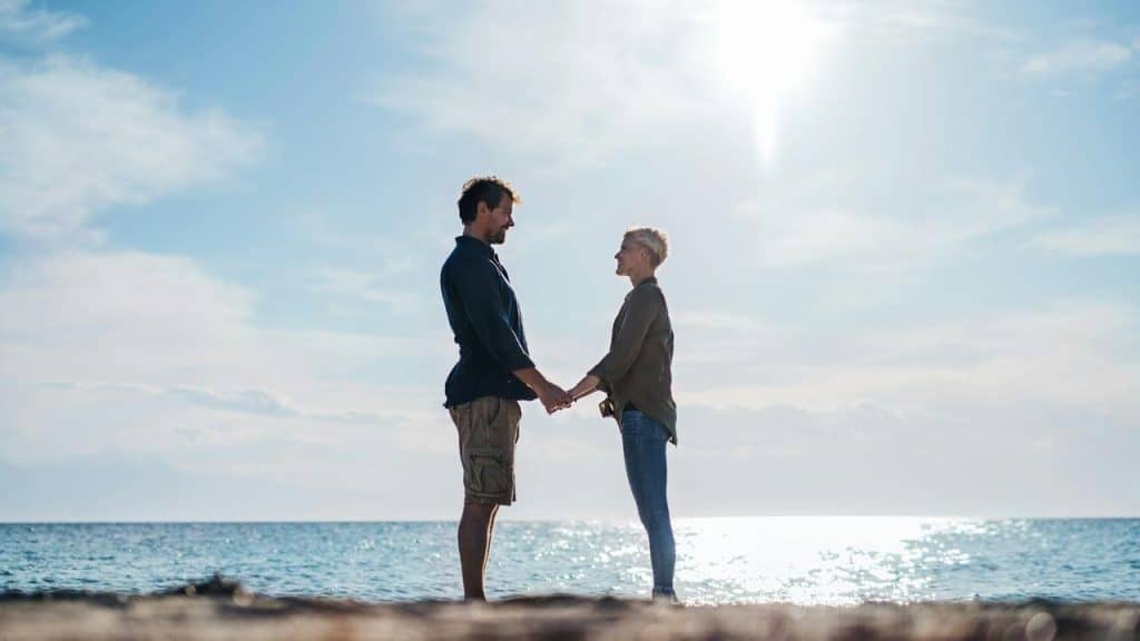 A couple holding hands by the sea under the sun.