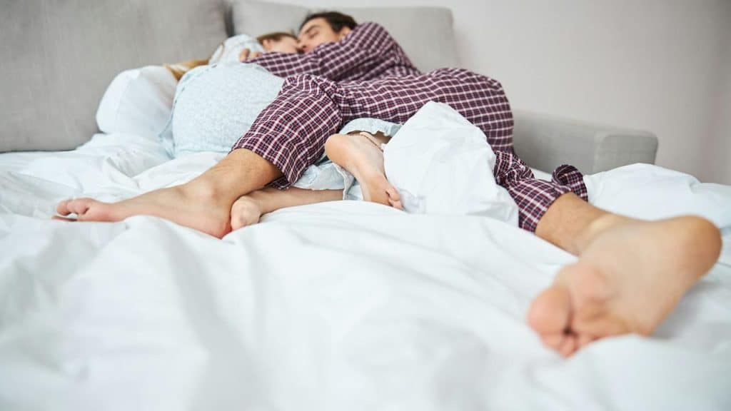 A couple cuddling in bed under white sheets.