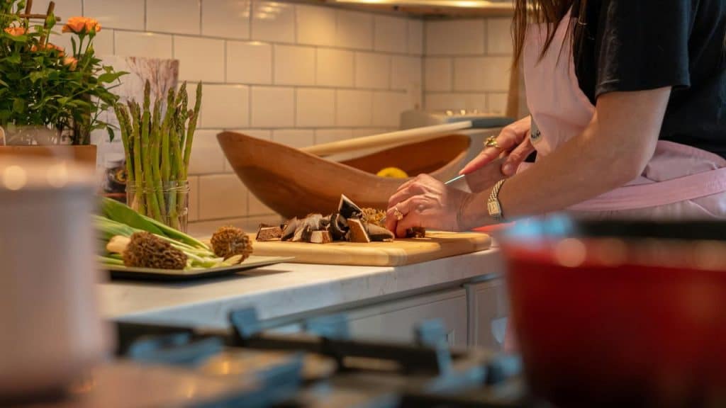 A person chops mushrooms on a cutting board in a kitchen.