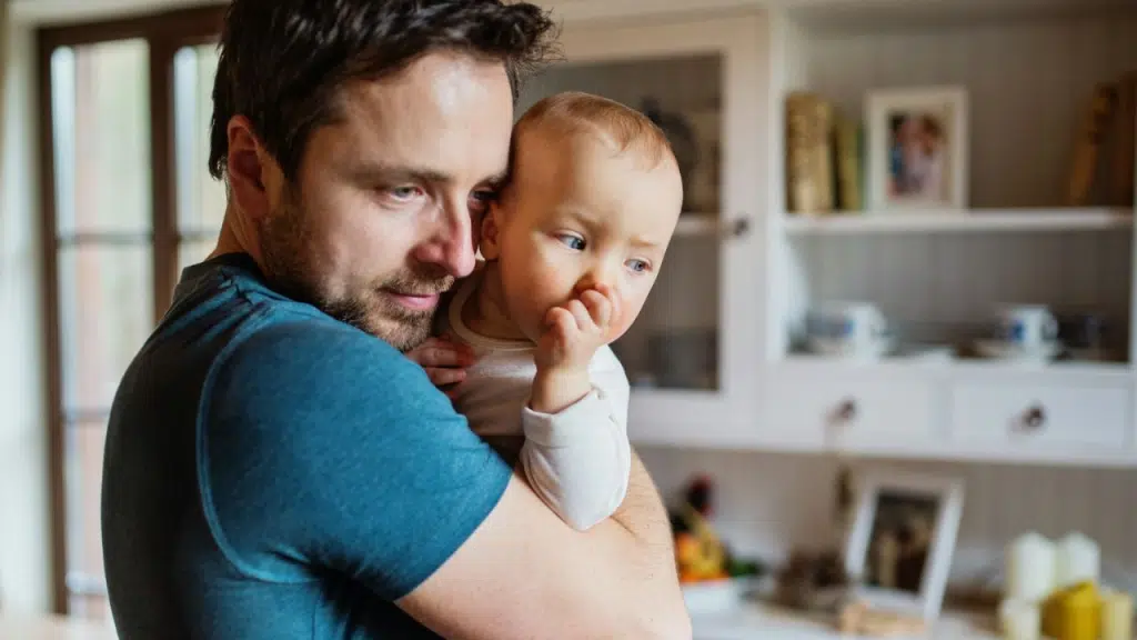 A man with a beard is holding and looking at a baby in his arms.