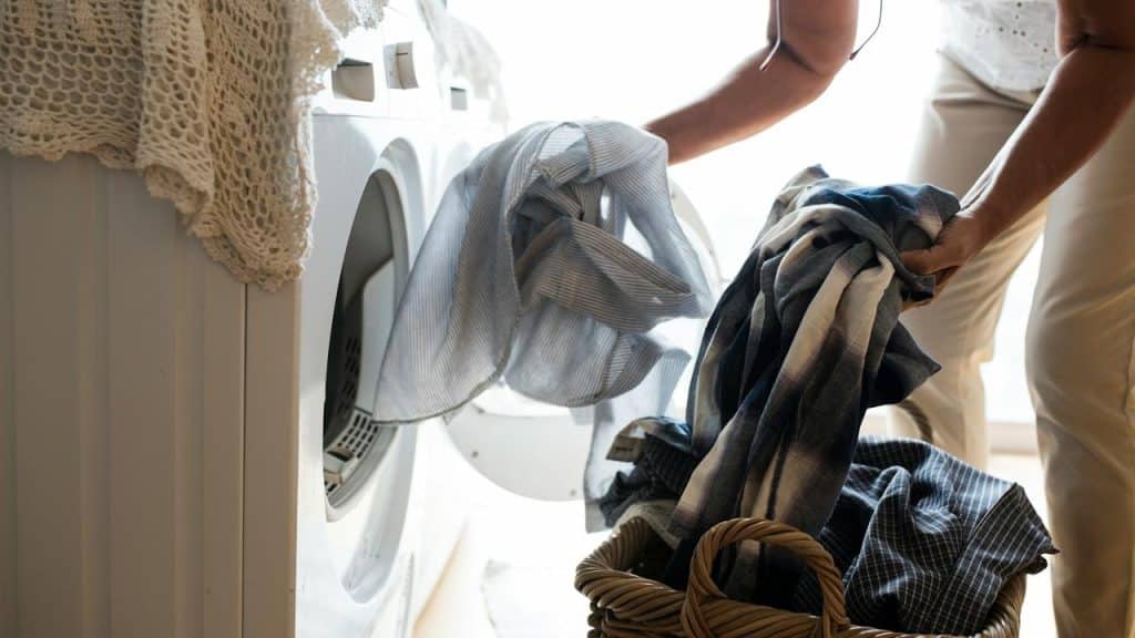 A person loads clothes into a washing machine from a laundry basket.