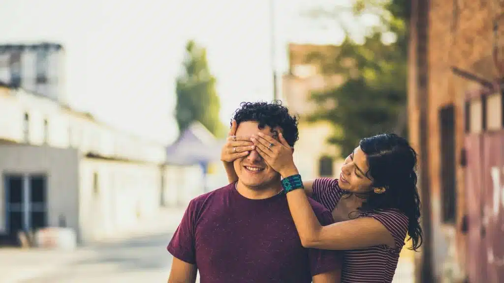A woman playfully covering a man’s eyes outdoors.