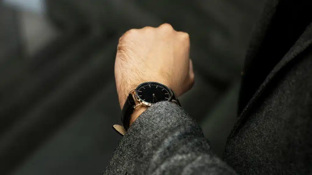 A man in a gray suit checking the time on a black wristwatch.