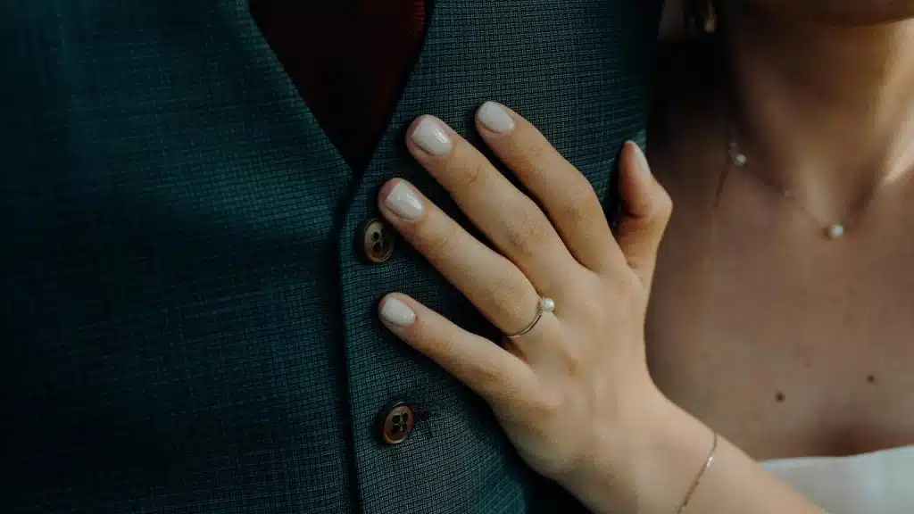 A woman’s hand with a pearl ring resting on a man’s suit chest.