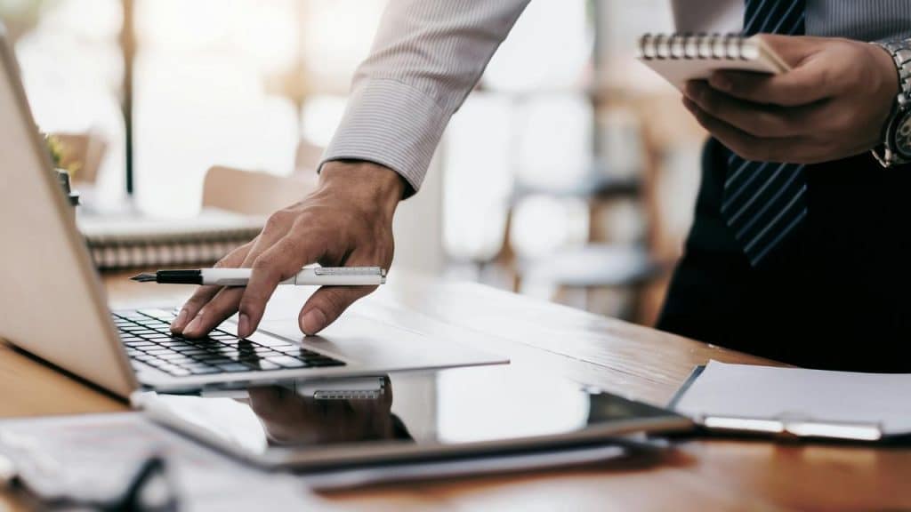 A person working at a desk with a laptop, notebook, and pen.