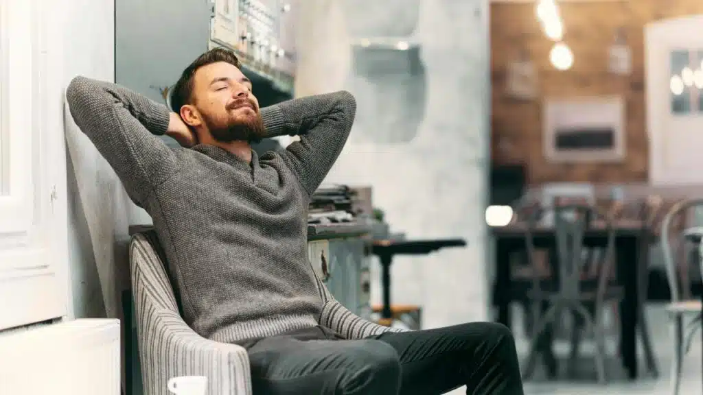 A man relaxing in a chair with his hands behind his head in a cozy room.