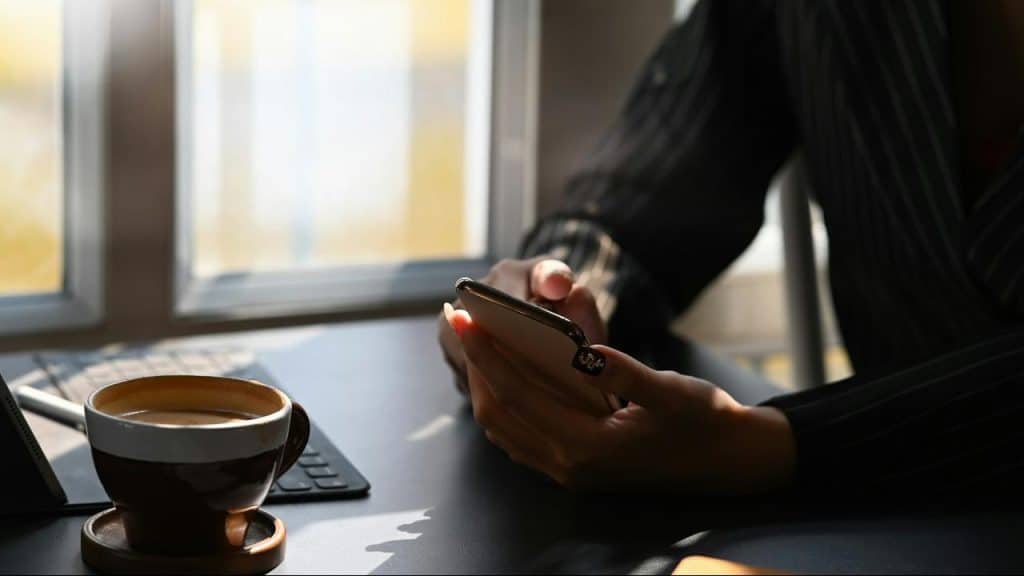 A person holding a smartphone at a table with a cup of coffee.