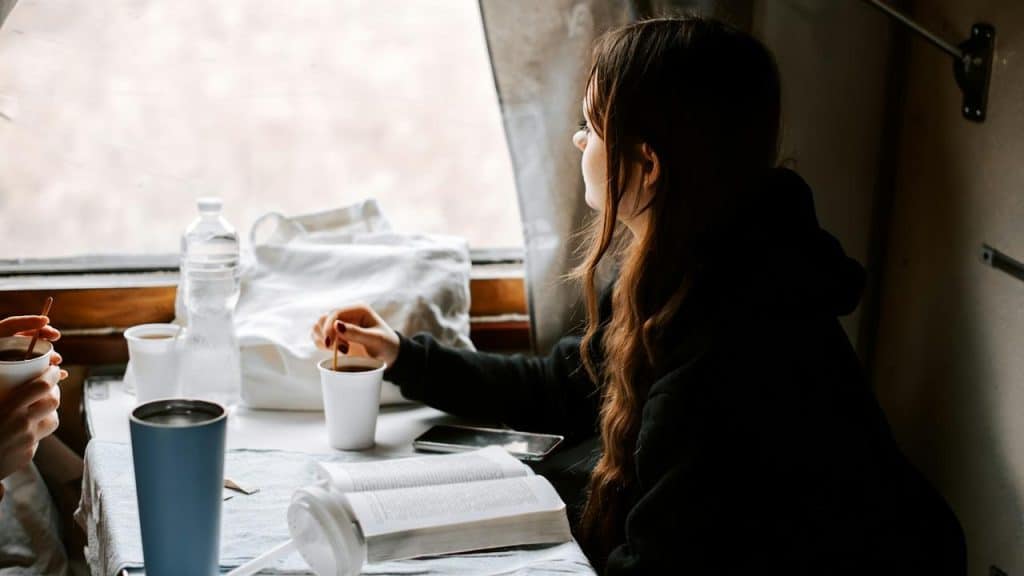 A woman sitting by a window with a cup of coffee and an open book.