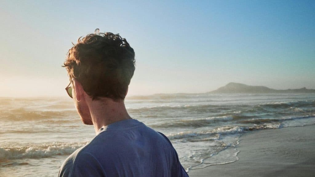 A man wearing sunglasses standing on the beach at sunset.