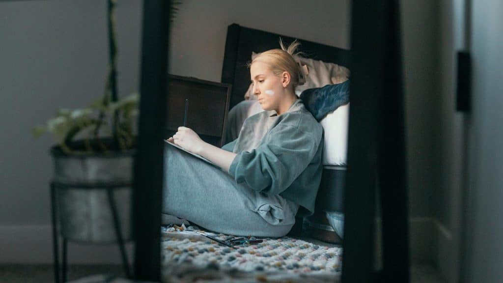 A woman sitting on the floor writing in a notebook.