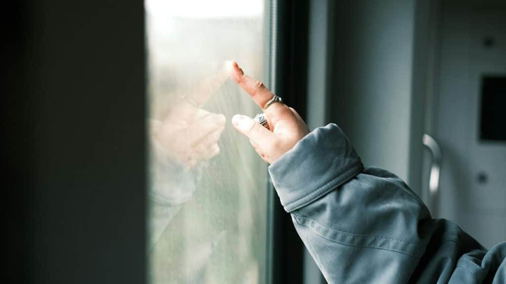 A person’s hand with rings touching a window.