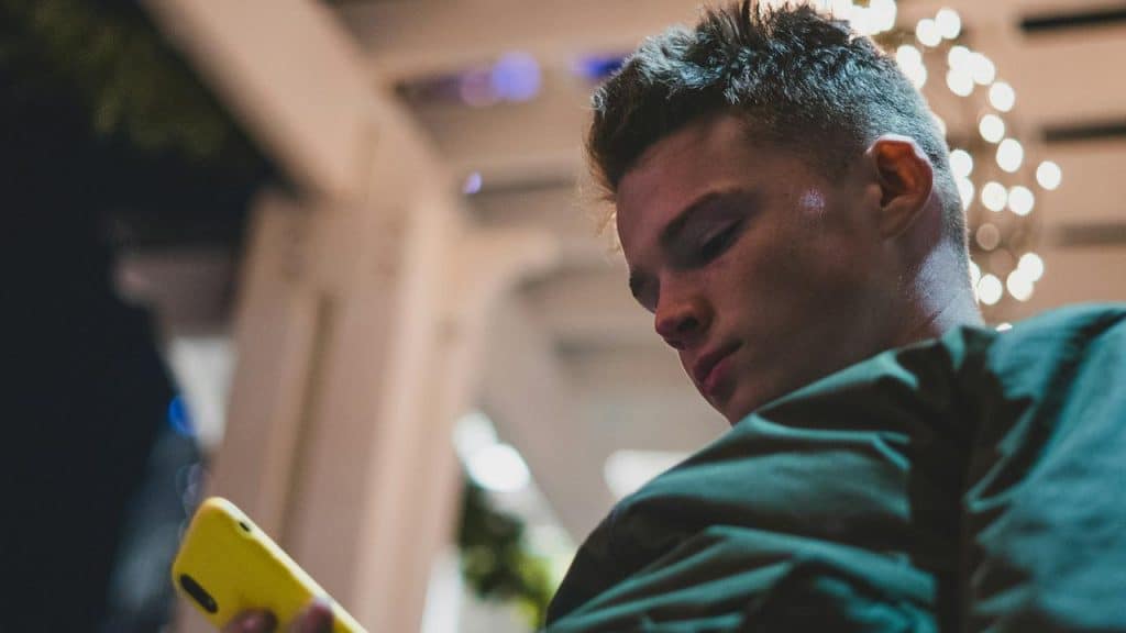 A young man looking at his phone with a yellow case at night.