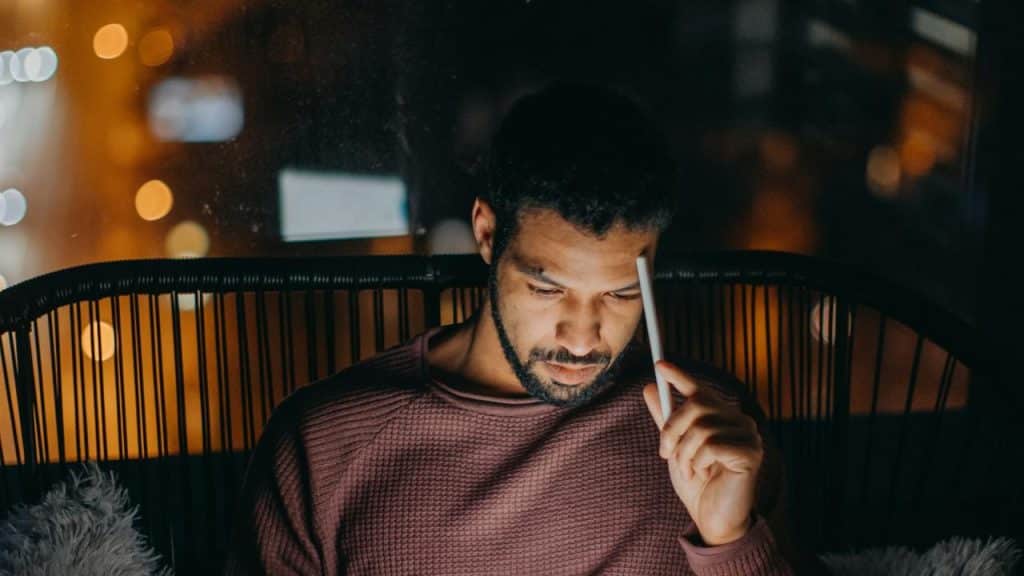 A man sitting at night holding a tablet pen while looking down.