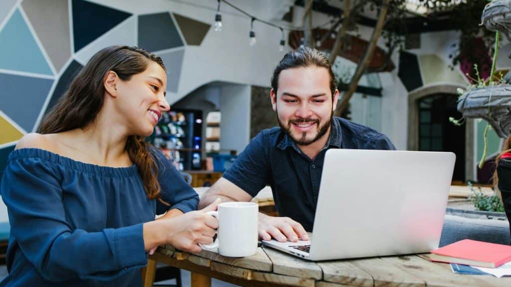 A man and woman smiling while looking at a laptop in a café.