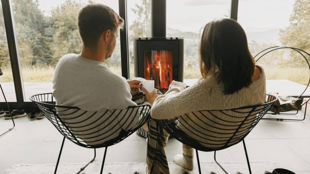 A couple sitting by a fireplace with coffee mugs.