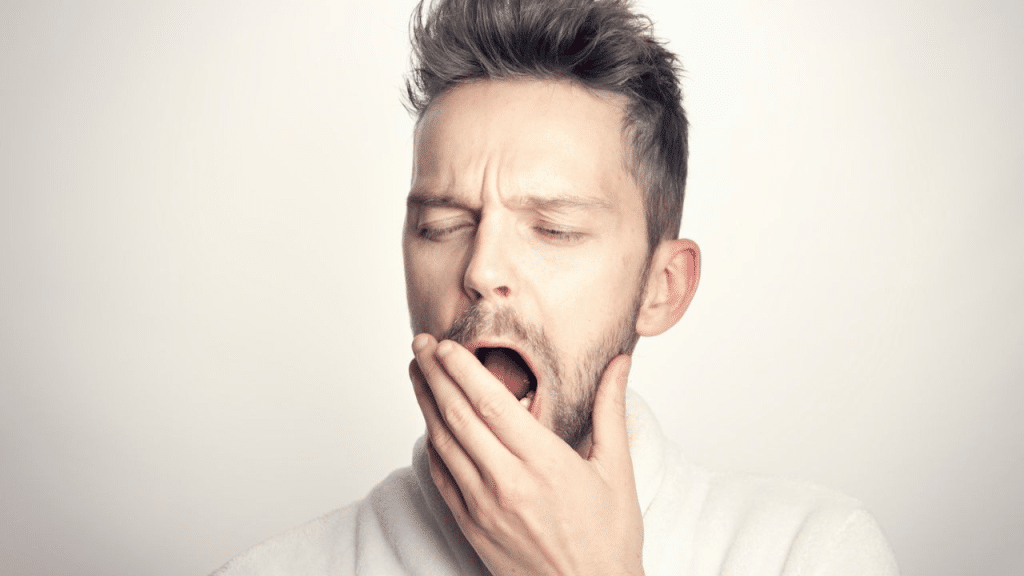 A man with his eyes closed and mouth open is yawning, with his hand on his chin.
