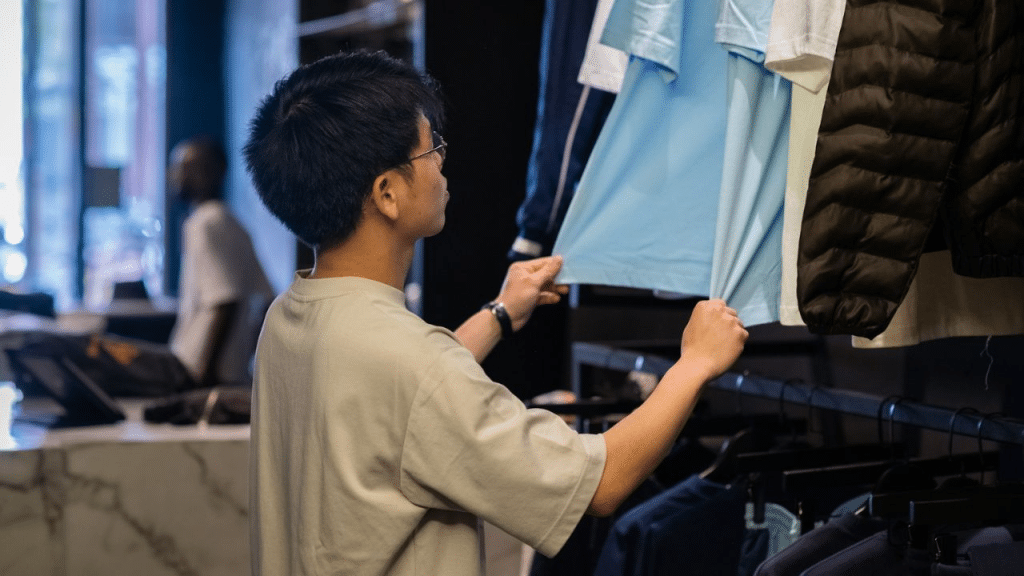 A person with glasses is looking at a light blue shirt hanging on a clothing rack.