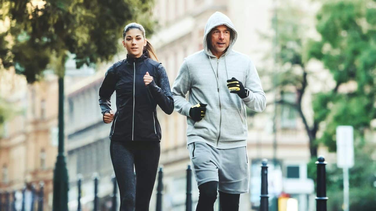 A woman and a man are jogging side by side down a city street in their workout clothes.