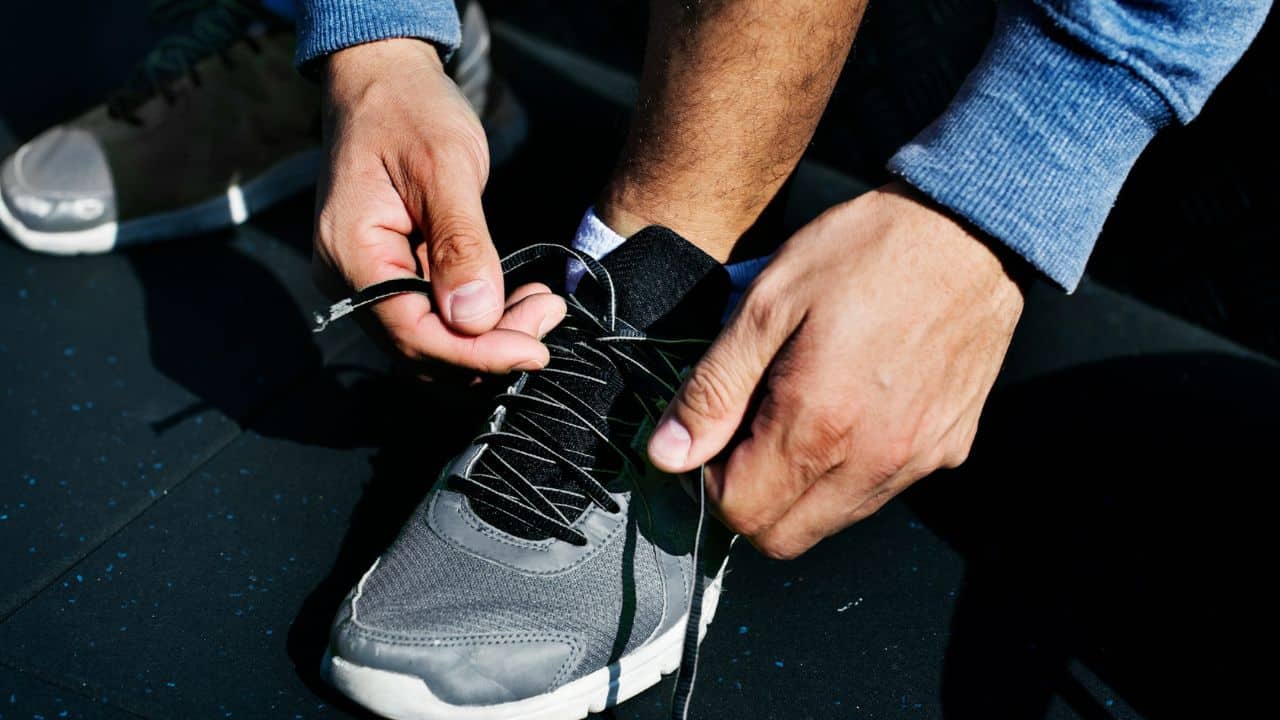 A person is sitting down and tying the laces of a grey and black athletic shoe.