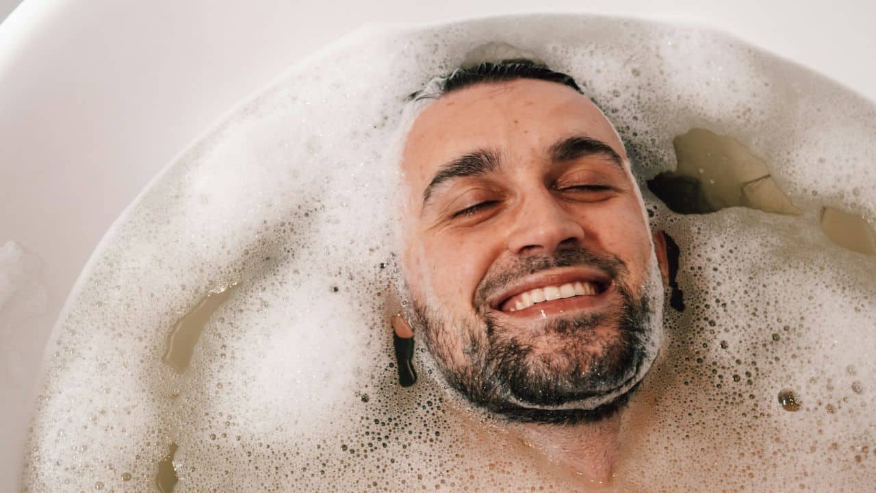 A happy man is smiling with his eyes closed while relaxing in a bubble bath.