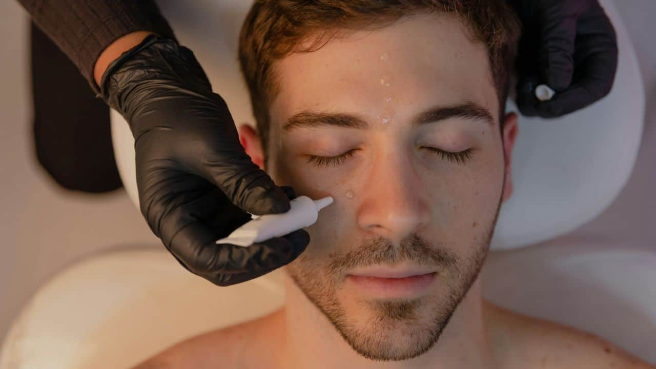 A person in black gloves is applying a product to a man's face during a spa treatment.