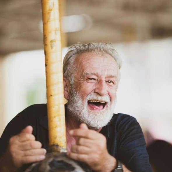 A senior man with a white beard is joyfully laughing, riding on a carousel.