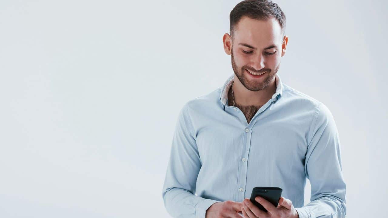 A happy man in a blue shirt is looking at his phone with a smile.