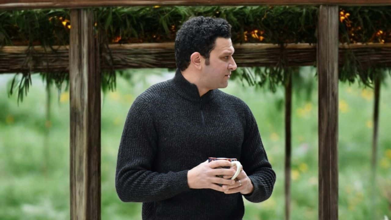 A man in a black sweater is holding a coffee mug and looking off to the side.
