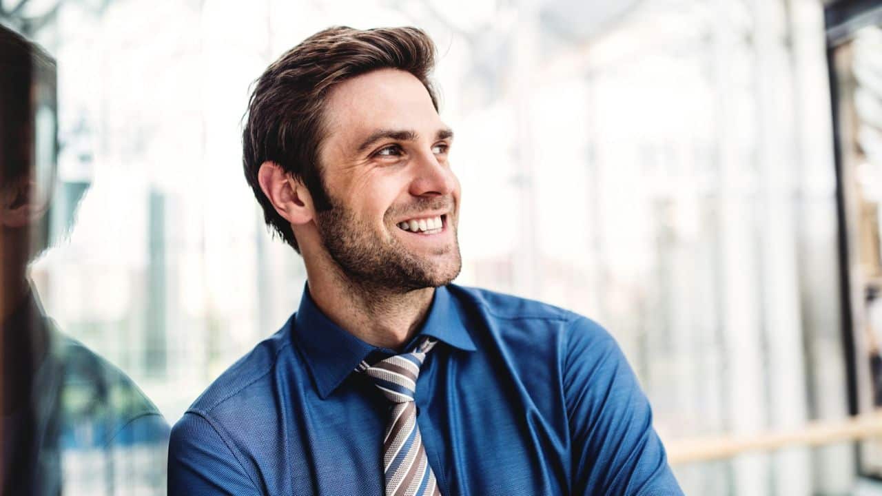 A happy businessman in a blue shirt and striped tie is smiling and looking to the side.