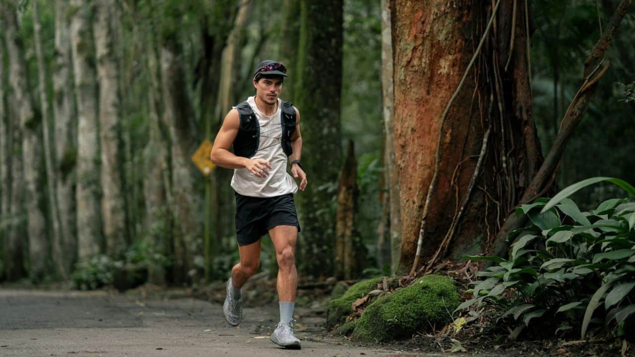 A handsome male athlete is jogging on a path through a dense, green forest.