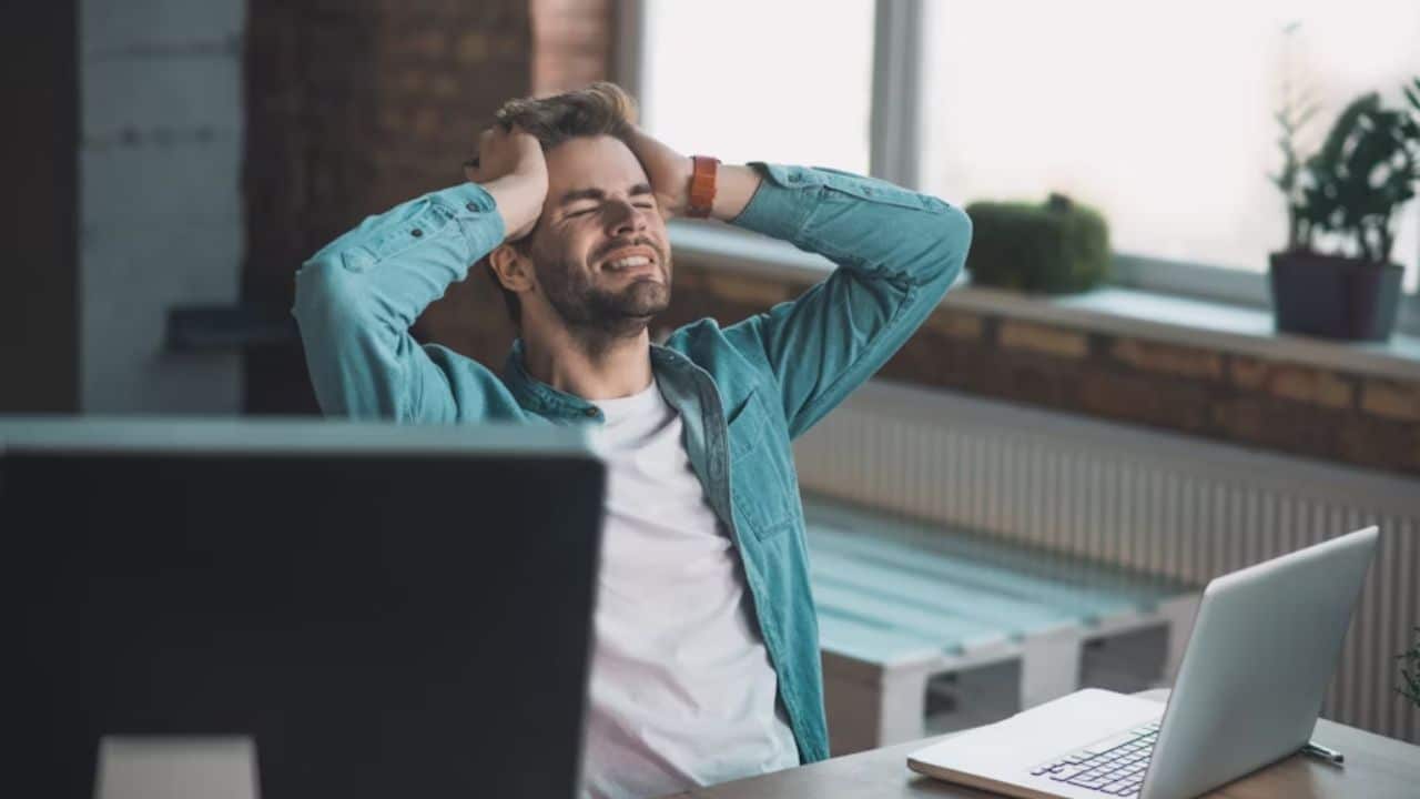 A man in casual clothes working at a desk, stressed expression.