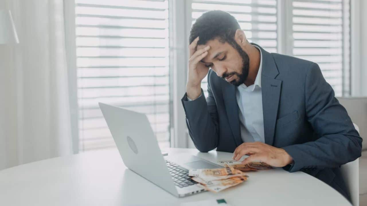 Man looking stressed while reviewing finances on laptop.