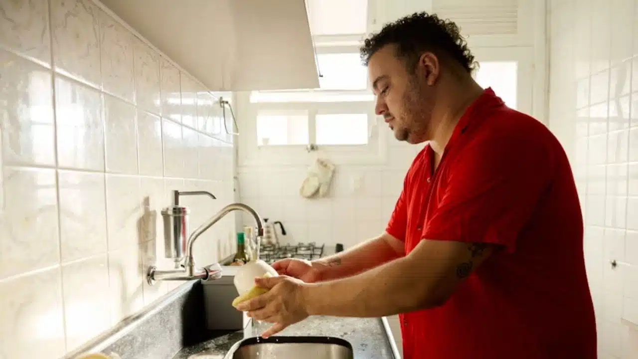 Man in casual clothes at kitchen sink washing dishes.