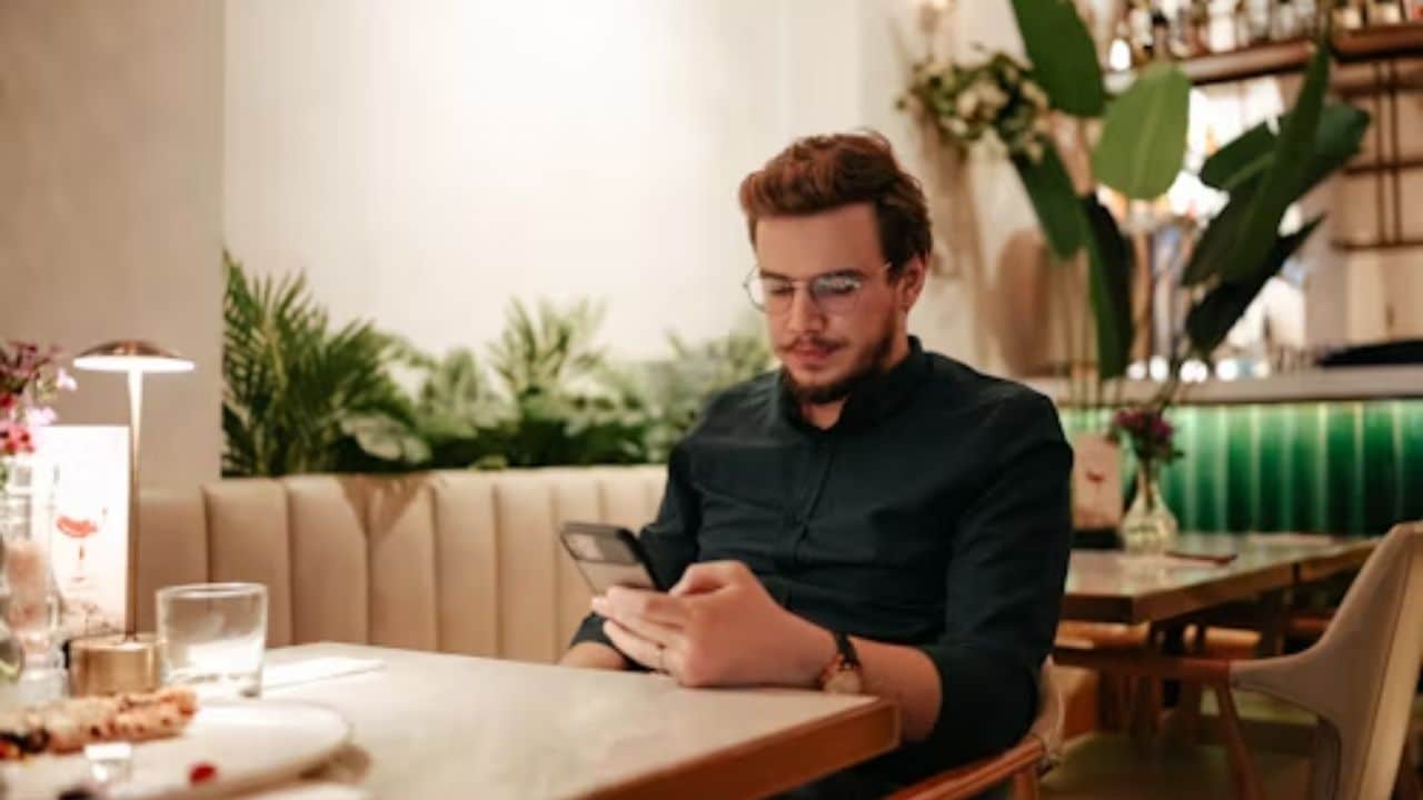 Man texting old friends while sitting alone at dinner table.