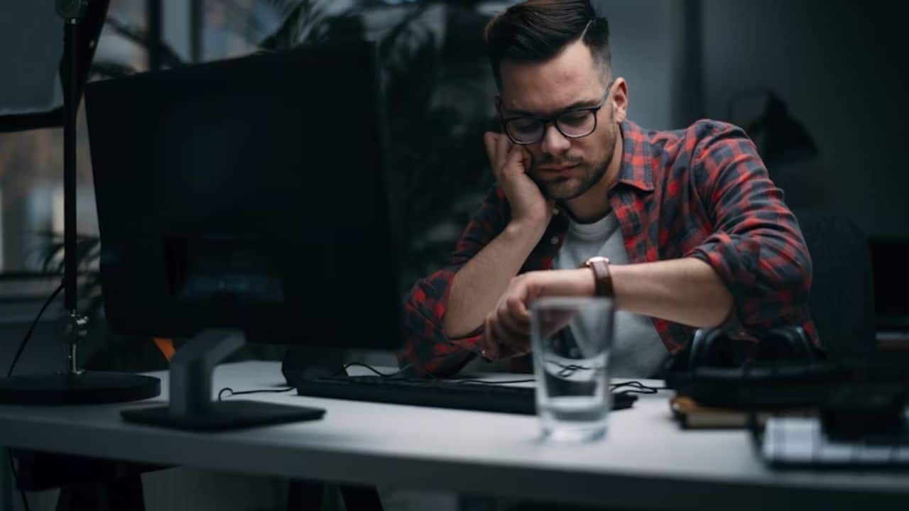 Tired man looking at his watch while working on computer at night.