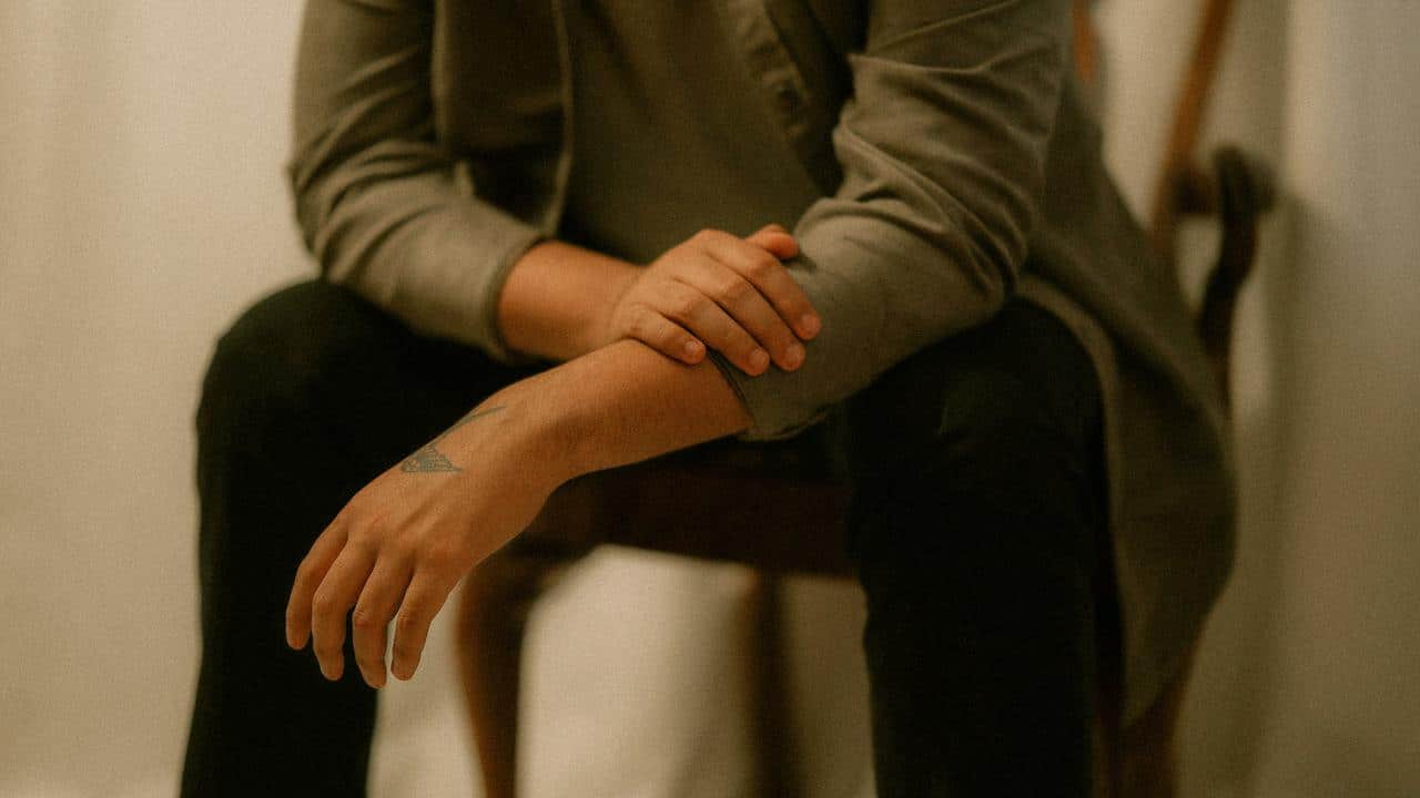A person sitting on a chair with arms crossed, showing a triangle tattoo on the forearm.