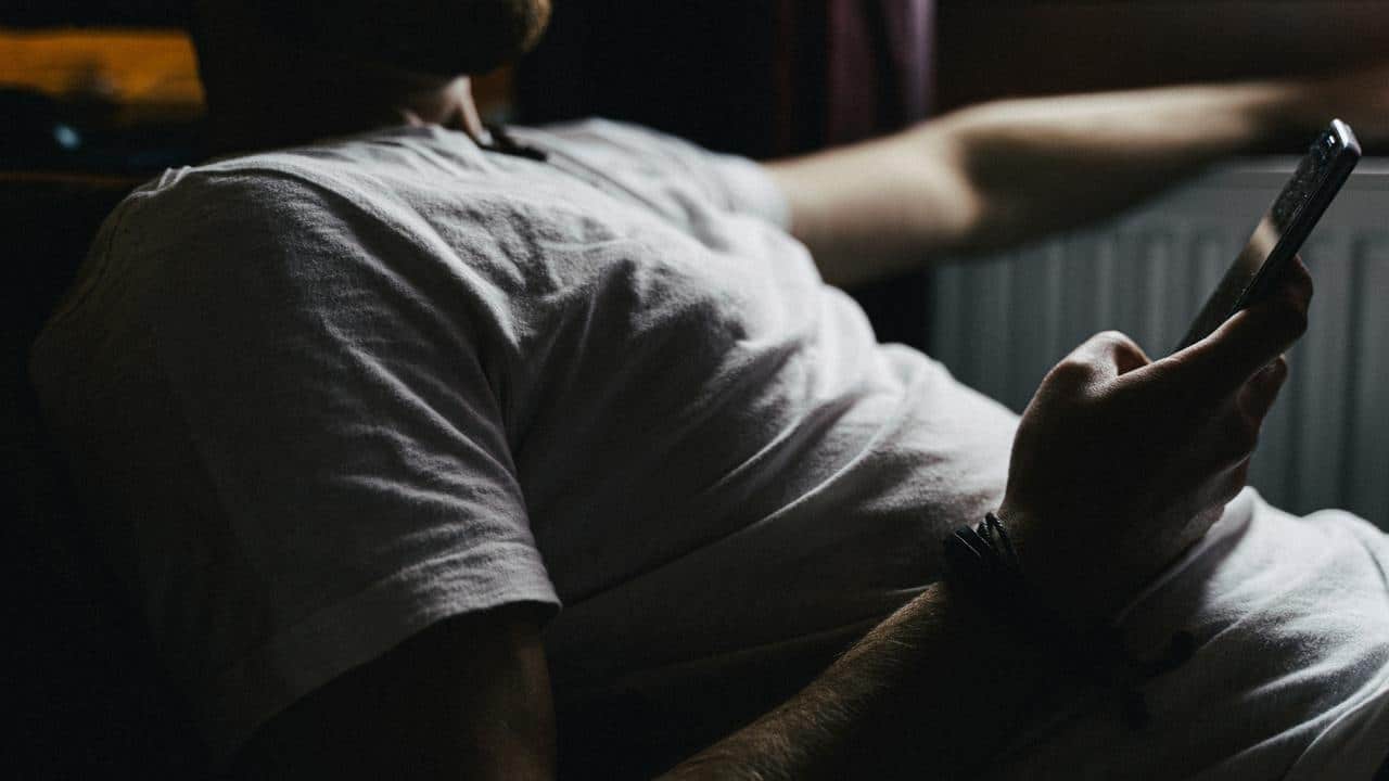 A person in a white t-shirt reclines while holding a smartphone.