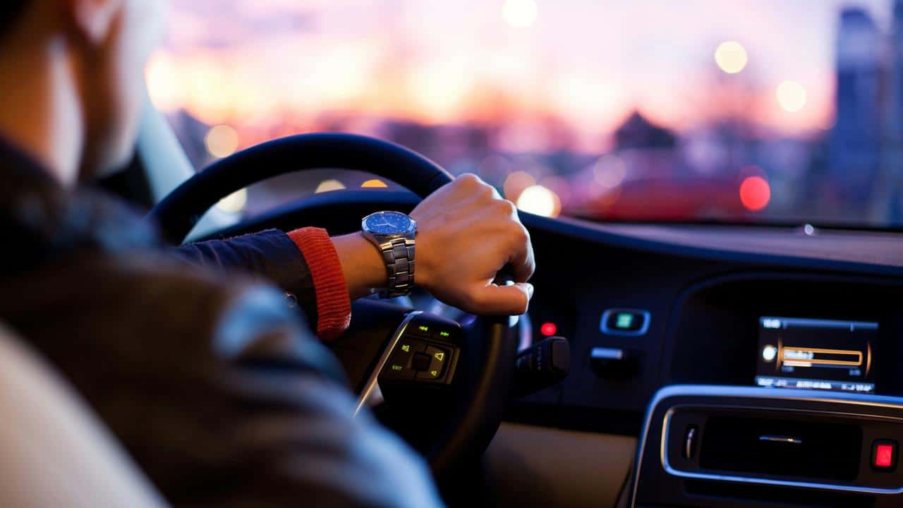 A person wearing a watch drives a car at sunset.
