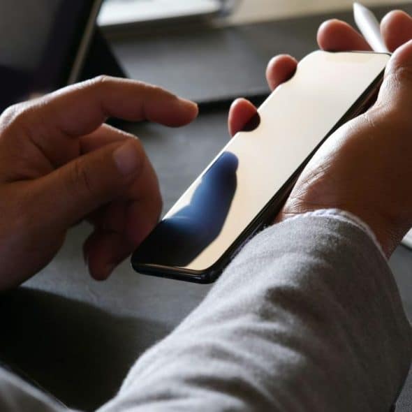 A person holding a smartphone and stylus while using a laptop and keyboard.