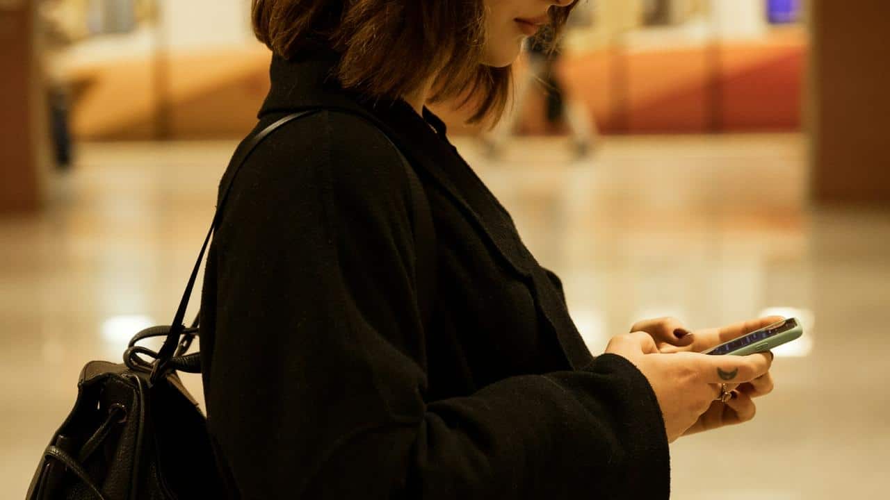 A woman in a black coat using her smartphone indoors.